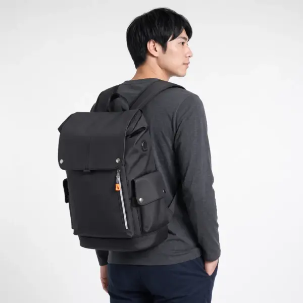 Black flap laptop backpack worn on one shoulder, side view